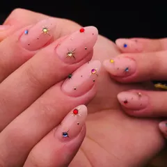 A galaxy of sparkle on your nails. This design uses a sheer pink base and is adorned with multi colored star shaped gems and tiny gold studs for a playful and celestial look.