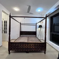 A classic four-poster bed frame made from dark, intricately carved wood. This showcases the quality of our custom furniture even before the room is fully dressed.