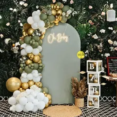 An elegant "Oh Baby" shower setup against a lush green wall. The sage green arched backdrop, neon sign, and organic balloon garland create a sophisticated and trendy look for the celebration.