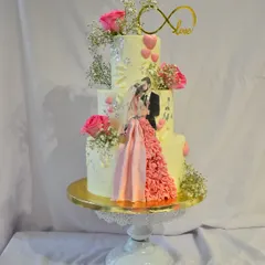 A three-tier engagement cake designed to capture a love story. This custom creation features an edible print of the couple, a flowing ruffled gown detail made of fondant, fresh pink roses, and an infinity love topper.