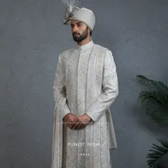 This complete ivory sherwani ensemble, with its matching stole and turban, blends historical opulence with modern sophistication. The detailed embroidery is designed for the groom who values cultural richness.