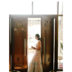 A grand entrance. The bride is framed by large wooden doors, creating a dramatic and beautiful portrait as she steps into her celebration.