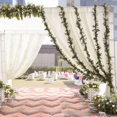 A beautiful daytime wedding entrance. The walkway features a chevron-patterned carpet and is framed by a grand arch of white drapes and lush green foliage.