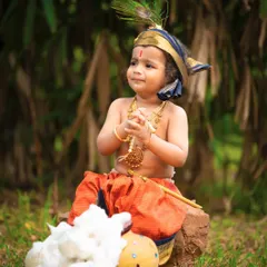 A playful little Krishna enjoying his butter in an outdoor setting. The natural greenery provides a beautiful backdrop that evokes the fields of Vrindavan.