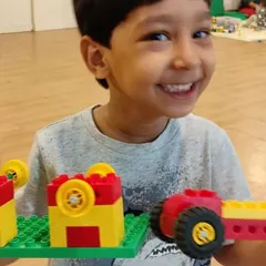 The proud smile of a young builder with his creation. He has built a tractor and wagon, showing great progress in his ability to follow instructions and build independently.