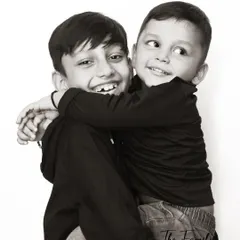 The playful energy between two brothers is perfectly captured in this black and white studio photograph. The simple white background puts all the focus on their expressions and interaction.