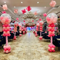 A grand walkway decoration for a large event. The hall is lined with elaborate pink balloon pillars, creating a stunning entrance for guests.