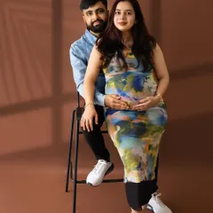 A contemporary couple's portrait with the mom-to-be in a colorful, abstract-print dress, seated on her partner's lap.