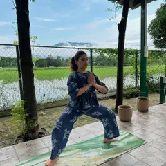 Practicing Virabhadrasana I, or Warrior I pose, during a yoga retreat in Dehradun. The beautiful natural surroundings with rice paddies and mountains enhance the experience.