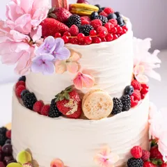 A full view of the stunning two-tiered cake, adorned with a cascade of fresh berries, macarons, and delicate flowers.