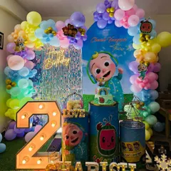 A vibrant Cocomelon themed party for Charish's second birthday, featuring a colorful balloon arch, a shimmery backdrop, and large character cutouts.