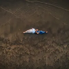 From above, we see a story of quiet connection. Lying on the wet sand as the waves retreat, this aerial view captures a serene, intimate moment, showing that love can be a peaceful escape from the world.