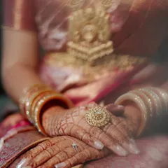 An artistic shot focusing on the bride's hands, adorned with intricate henna, traditional bangles, and a stunning statement ring, highlighting the rich details of a South Indian bridal look.