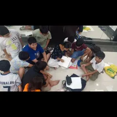 An instructor sits on the floor with a group of students, providing hands-on guidance for a drawing project. This collaborative and informal setting encourages open communication and learning.