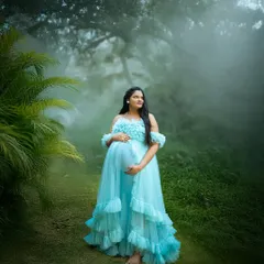Surrounded by mist and lush greenery, this mom to be looks like a forest queen. The vibrant blue gown contrasts beautifully with the natural setting, creating a stunning visual.