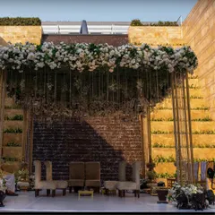 A grand mandap setup at the Grand Hyatt Mumbai, featuring a stunning overhead floral installation against a dramatic stone wall.