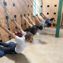 A closer look at students exploring different supported poses on the rope wall. This practice is beneficial for all levels, helping to build awareness and decompress the spine.
