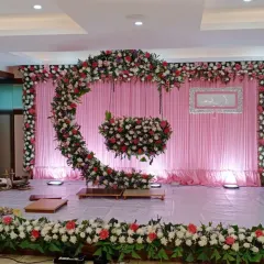 A unique crescent-shaped floral arrangement for a naming ceremony. The cradle is designed to look like it's hanging from the moon, decorated with pink, white, and red flowers for a magical touch.