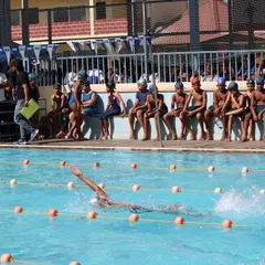 A swimmer powers through the water during the backstroke event at the Sportonix Anniversary Cup 2024, with parents cheering from the sidelines.