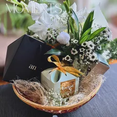 A styled moment in a basket. This arrangement combines a fresh bouquet of white gladiolus and daisies with elegantly packaged gifts, perfect for a sophisticated festive celebration.