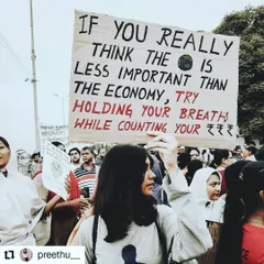 A protestor in India holds a sign that reads, "If you really think the Earth is less important than the economy, try holding your breath while counting your money." It's a sharp, witty, and profound statement on our priorities.