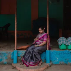 A quiet moment of reflection on the porch of a traditional village home. The vibrant colors of the wall and her saree create a beautiful, authentic scene.