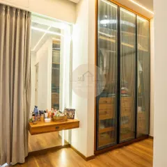 This walk-in closet area features a fluted glass wardrobe that offers a glimpse of the contents while keeping them dust-free. Paired with a floating dressing table and backlit mirror, it creates a dedicated and elegant space for getting ready.