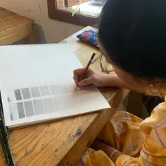 A student practices creating value scales with a pencil. This fundamental exercise teaches control over pressure and tone, which is crucial for realistic shading.
