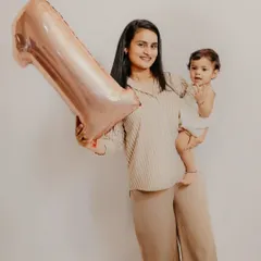 A proud mother holds her baby and a "1" balloon to celebrate her child's first birthday milestone.