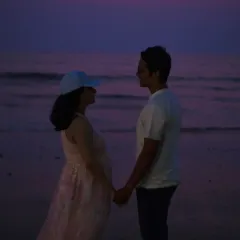 A stunning twilight shot of the couple holding hands on the beach, silhouetted against a beautiful purple and pink sky.
