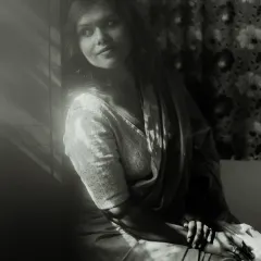 A classic black and white window-lit portrait. The play of light and shadow across the model's face and clothing creates a timeless, cinematic feel, full of quiet contemplation.