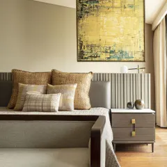 The master bedroom at the Jor Bagh Residence features a captivating hanging artwork that demarcates the bed and study space. Textured pillows and neutral quilts create a serene and personal retreat.