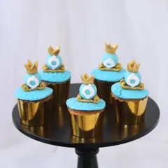 These Cinderella-themed cupcakes are perfect for a fairytale birthday party. Each one is topped with intricate, handcrafted fondant details, including delicate blue frosting and edible gold crowns, all presented in elegant gold foil liners.