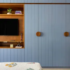 This bedroom wardrobe features fluted panels in a calming blue, with custom circular wooden handles. The design also cleverly integrates a niche for the TV, saving space and creating a clean, cohesive look.