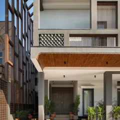 The entrance sequence softens the building's rugged exterior. Earthy terracotta pots and lush greenery guide the approach, while towering columns and a wooden soffit frame the main door, creating a transition from the industrial cityscape to a serene residential space.