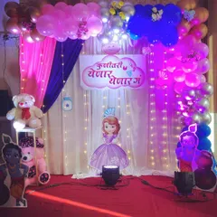 A full stage setup for a baby shower, combining a balloon arch, drapes, fairy lights, and character cutouts for a magical theme.