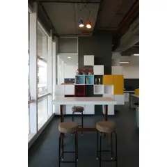 A high table by the window provides an alternative workspace. The design uses 'pixels' of storage in primary colors, a nod to the 8-bit gaming theme that runs through the entire office.