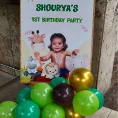 A personalized welcome sign for a jungle-themed first birthday party. The sign features a photo of the birthday boy, cute animal graphics, and a small balloon arrangement at the base.