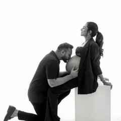A beautiful expression of love. The father-to-be's kiss on the baby bump is a classic, heartfelt moment, styled in a chic and modern way with matching black outfits.