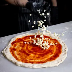 Next comes the cheese. Here, I'm scattering fresh, diced mozzarella over the tomato sauce. Using high-quality cheese that melts perfectly is key to getting that delicious, stringy texture every pizza needs.