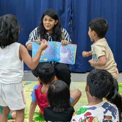 An instructor captivates the children with an illustrated storybook. You can see the excitement and curiosity on their faces as they interact with the story, shouting out answers and acting out the scenes.