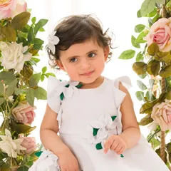 A sweet and thoughtful expression from a little girl in a white dress, surrounded by flowers. A quiet moment captured during her portrait session.