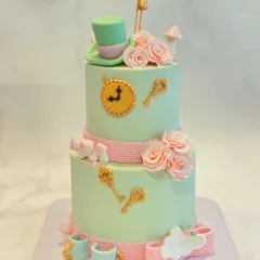 An "Alice in Wonderland" themed two-tiered cake. This whimsical creation includes iconic elements like the Mad Hatter's hat, a clock, keys, and teacups, all handcrafted from fondant.