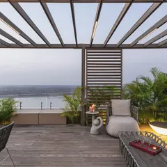 This duplex terrace in Surat offers an oasis of contemporary calm with expansive views of the Tapi River. We designed this outdoor space as a seamless extension of the interior, using a wooden pergola and minimalist furniture to create a sophisticated area for relaxation and entertainment, blurring the lines between inside and out.