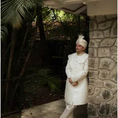 A full-length portrait of the groom leaning against a stone wall. His relaxed yet elegant pose captures a moment of quiet confidence before the ceremony.