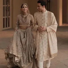 A portrait of pure elegance, this couple radiates charm. The groom is dressed in a classic beige sherwani with delicate embroidery, perfectly complementing the bride's embellished lehenga for a sophisticated wedding look.