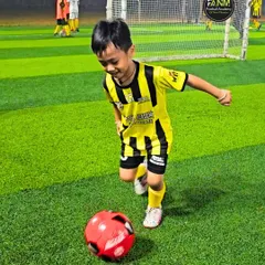 The joy of the game starts here. A young player runs with a smile on his face, chasing a bright red ball during a fun drill.