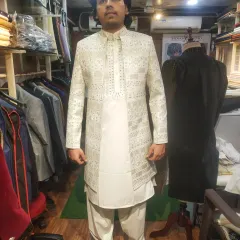 This client is seen in a custom-made off-white achkan set. The open-front jacket features intricate mirror work, worn over a simple kurta and salwar, demonstrating how we tailor traditional Indian groomswear to your exact measurements.