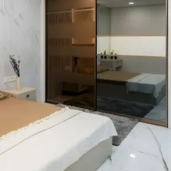 This tinted glass sliding wardrobe offers a sophisticated way to store your belongings. The semi-transparent doors, paired with fluted wall panels and soft lighting, create a luxurious and serene bedroom retreat.
