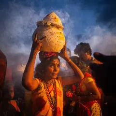 A woman carries a sacred pot on her head through a cloud of smoke, her expression a mix of determination and devotion during the Kulasai procession.